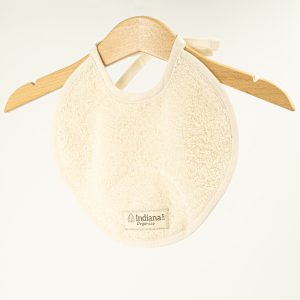 Babero beige de algodón orgánico Indiana 1727 colgado en percha de madera.